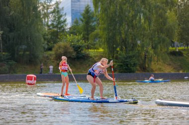 Bir çocuk sörf tahtasının üzerinde yüzüyor, kürekle itiyor. Paddleboard.