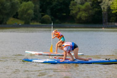 Bir çocuk sörf tahtasının üzerinde yüzüyor, kürekle itiyor. Paddleboard.