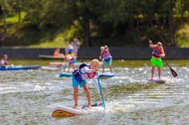 Bir çocuk sörf tahtasının üzerinde yüzüyor, kürekle itiyor. Paddleboard.
