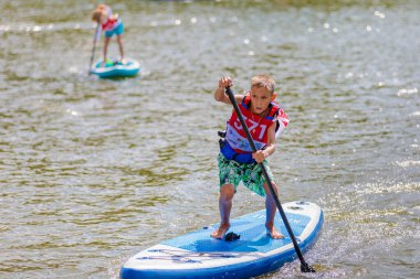 Bir çocuk sörf tahtasının üzerinde yüzüyor, kürekle itiyor. Paddleboard.