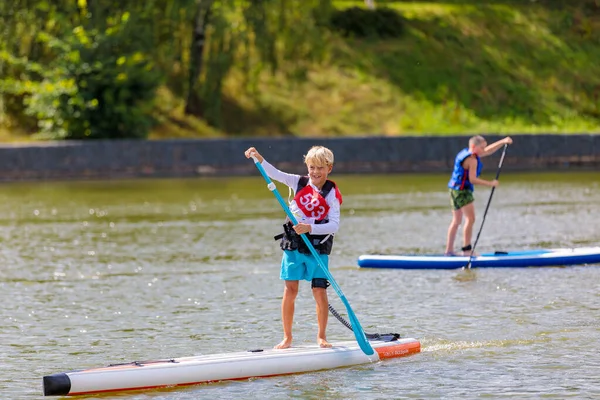 Un niño nada en una tabla de surf, empujando con una pala. Paddleboarding. —  Fotos de Stock