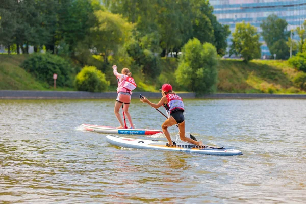 A child swims on a surfboard, pushing off with a paddle. Paddleboarding. — Stock Photo, Image
