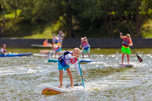 A child swims on a surfboard, pushing off with a paddle. Paddleboarding. — Stock Photo, Image