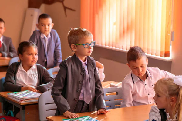 The first grader stands at the desk and answers the teachers question. — Stock Photo, Image