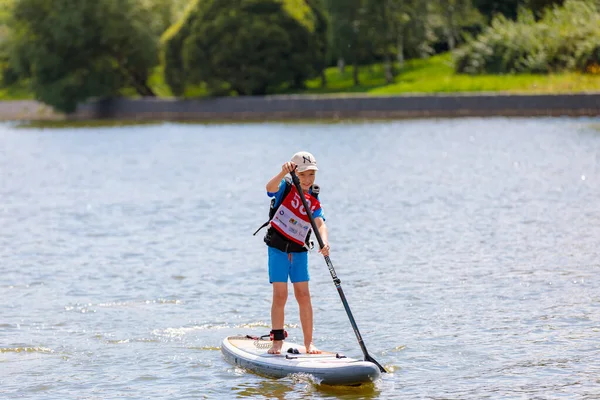 A child swims on a surfboard, pushing off with a paddle. Paddleboarding. — Stock Photo, Image