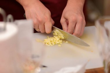 Mans elleri akşam yemeği hazırlamak için sarımsak kesiyor. Sarımsağı mutfak bıçağıyla doğrayın..