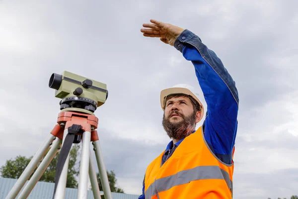 Stavební inženýr s optickou úrovní mávne rukou, aby ovládl kolegy z dálky. — Stock fotografie