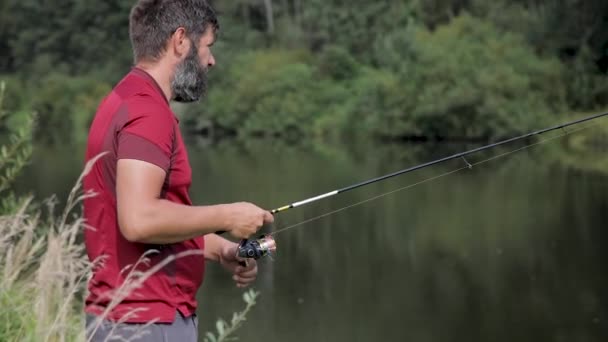 Een man met een baard vist op de rivier en werpt een lijn.. — Stockvideo
