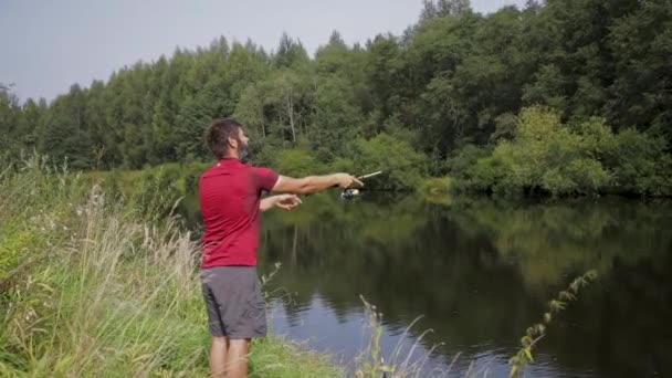 Um homem com barba está pescando no rio, lançando uma linha. — Vídeo de Stock
