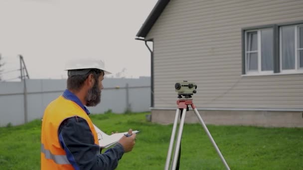 Egy férfi mérnök a helyszínen optikai szinttel dolgozik.. — Stock videók
