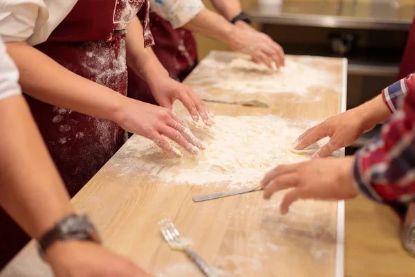 Le mani di più persone stanno impastando l'impasto sul tavolo. Mescolare un uovo crudo con farina. — Foto Stock