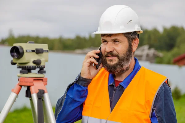 Stavební inženýr s optickou úrovní mluvící na mobilním telefonu. — Stock fotografie