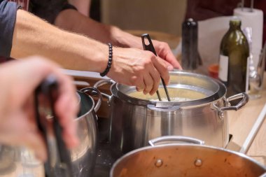 Şef büyük metal tavalar içinde makarna hazırlar. Erkek eller makarnayı maşayla tavadan çıkarır. Yakın plan..