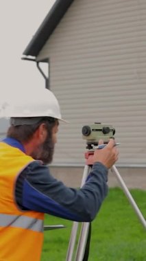 Erkek bir mühendis optik seviyede çalışıyor. Miğferli bir müteahhit optik bir cihaza bakar..