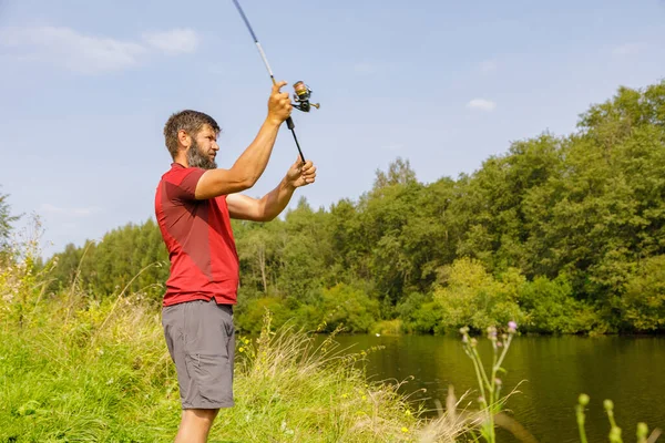 髭を生やした男が川で釣りをしている 釣竿を持った漁師が川岸で釣りをしている — ストック写真