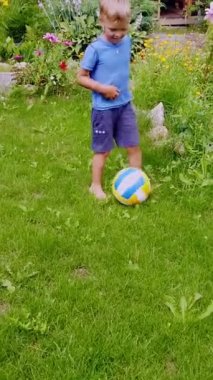 Yeşil çimlerde futbol oynayan bir çocuk. Çocuk çimenlerde yalın ayak koşar ve topa vurur..