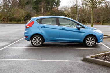 Hampshire, England, UK. 2021. Small blue saloon car on a parking lot on a wet day. clipart