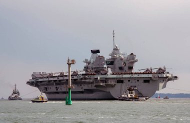 Portsmouth, İngiltere, İngiltere. 2021 yılı. HMS Kraliçesi Elizabeth, eskort gemileri taşıyan bir uçak gemisi Portsmouth Limanı 'ndan açık denize doğru hareket ediyor..