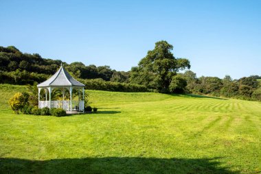 Güney Devon, İngiltere, İngiltere. 2021 yılı. İngiliz kırsalında çevresindeki çalılarla çevrili bahçe çardağı.