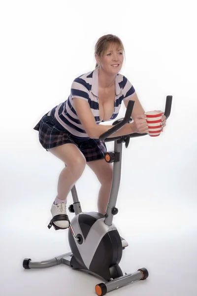Woman on exercise bike with a mug of tea — Stock Photo, Image