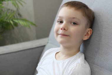 7-8 yaşlarında beyaz tişörtlü, gülümseyen sevimli bir çocuk. Açık beyaz gri nokta