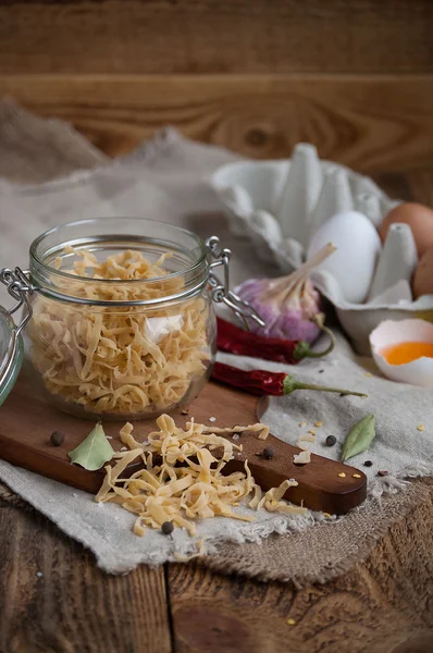 Rustik mutfak masasında yumurta, zeytinyağı, biber, sarımsak, kesme tahtası ve baharatlar ile ev yapımı makarna