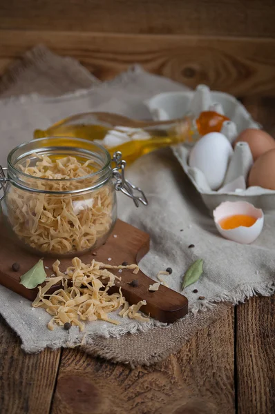 Rustik mutfak masasında yumurta, zeytinyağı, kesme tahtası ve baharatlar ile ev yapımı makarna
