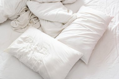 Top view of an unmade bed in a bedroom with crumpled bed sheet, a blanket, a white shower towel and two pillows. clipart