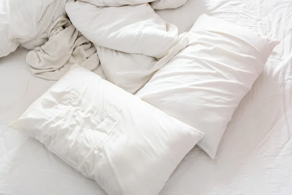 Top view of an unmade bed in a bedroom with crumpled bed sheet, a blanket, a white shower towel and two pillows. — Stock Photo, Image