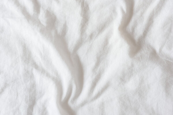 Top view of creased / wrinkles on a white unmade / messy bed sheet.