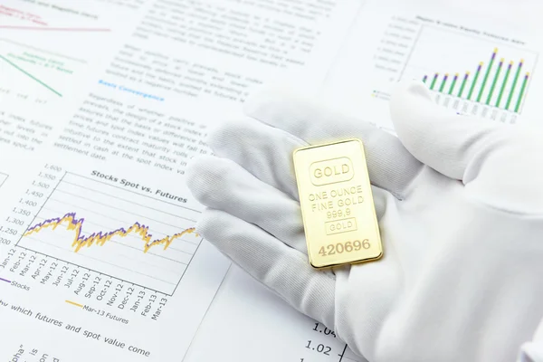 Man rechterhand met een witte handige handschoen toont/presenteert een one ounce Gold Bar aan een klant voor inspectie. Stockfoto