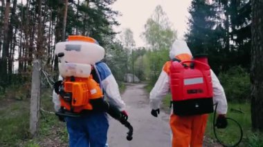 Koruyucu giysiler içindeki epidemiyologlar parkta yürürler.