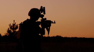 Silahlı bir askerin silueti. Tüfeği ve gece görüş teçhizatıyla gün batımına karşı. Askeri eğitim ve taktik operasyon