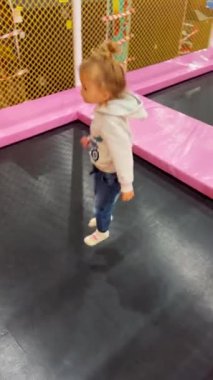 Çocukların oyun merkezinde trambolinde zıplayan neşeli küçük kız. Aktif güvenli eğlence, aile eğlencesi ve sağlıklı hareket
