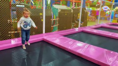 Küçük bir kız renkli bir oyun merkezinde trambolinde neşeyle zıplıyor. Eğlenceli çocuk aktivitesi, enerjik hareket, çocuklar için güvenli eğlence alanı