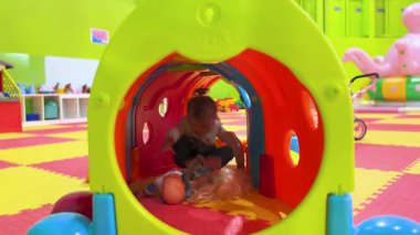 Küçük çocuk, kapalı bir çocuk parkındaki parlak plastik bir tünelde emekliyor. Eğlence aktivitesi, güvenli ortam, erken gelişim ve aile eğlencesi