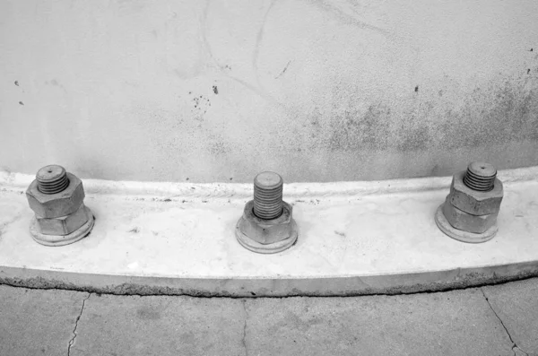 Three iron studs (bolts) with tightened nuts and washers. Part of concrete and metal of old street construction. Black and white background.