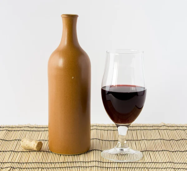 Seramik şişe ve bir kadeh kırmızı şarap bir bambu hasır üzerinde