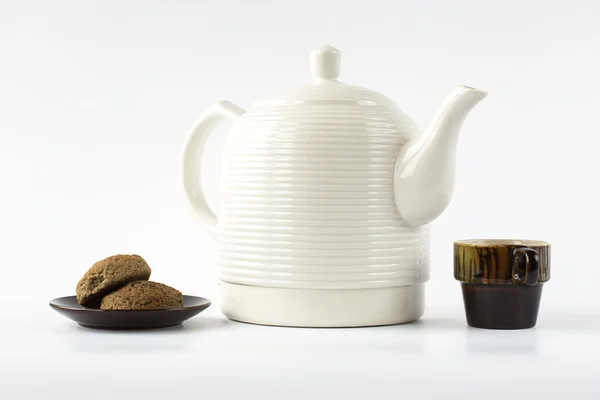 Bir tabak kurabiye ve üzerinde seramik su ısıtıcısı ile iki seramik bardak 