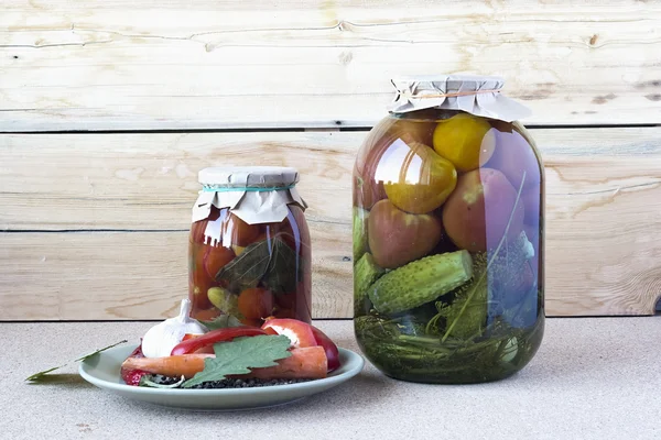 Tomates salées et concombres dans une banque de verre avec des épices sur un — Photo