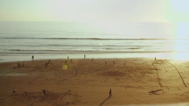 Sylwetka ludzi na plaży Oceanu Atlantyckiego w zwolnionym tempie, osoby grające w piłkę nożną na plaży o zachodzie słońca, wybrzeże Taghazout, Maroko, 4k — Wideo stockowe