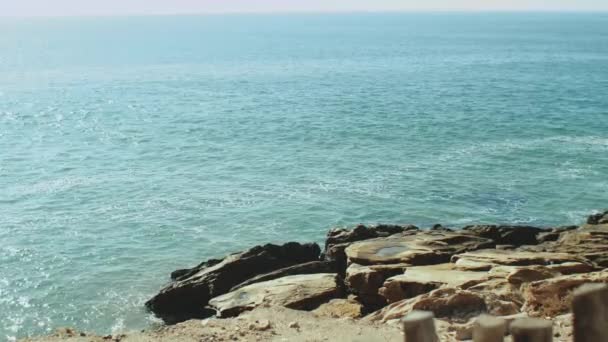 Медленное движение, Атлантический океан вода во время прилива врезаться в каменистый берег, волны ударил камни слегка, солнечная погода и ясное небо, Марокко 4k — стоковое видео