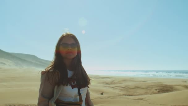 A mulher de óculos de sol olha para o horizonte oceânico. Amazing Sand Dunes by Beautiful Blue Ocean, Dahkla, Marrocos, coelhos do sol na câmera, câmera lenta, 4k — Vídeo de Stock