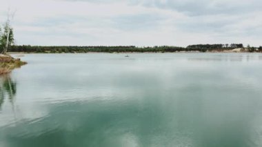 Yeşil orman ve göl kıyısının havadan görünüşü. Gölün ortasında yapayalnız bir tekne, çam ağacı ormanıyla yazlık doğal göl manzarası. Ukrayna doğası, güzel göl ve yeşil orman üzerindeki hava.