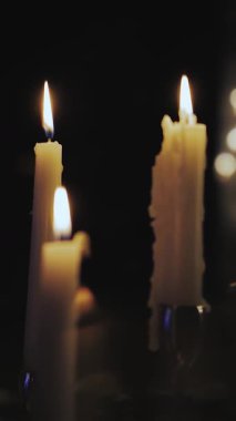 Dikey video. Siyah arka planda yanan mumlara yakın plan. Mum ışığında akşam yemeği. Pastel renkli masa dekoru. Düğün ya da doğum günü. Yüksek kalite 4k görüntü