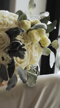 Dikey video. Gelin elinde bir buket beyaz gül, düğün sabahı, düğün hazırlıkları. Ağır çekim. Yüksek kalite 4k görüntü