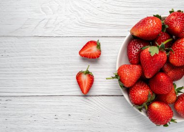Tahta masadaki beyaz kasede taze çilekler. Vejetaryen yemeği. Kopyalama alanı olan üst görünüm. sağlıklı gıda konsepti