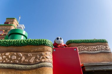 NOV 27 2025 Universal Studios Japan: Eğlence parkında parlak bir gün renkli bir slayt ve tepenin arkasından bakan neşeli bir karakter