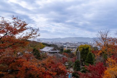 NOV 28 2025 Kiyomizu-dera, Japonya: Kyoto 'nun renkli yaprakları ve bulutlu bir gökyüzü altında uzak dağları olan tepedeki tapınağın sonbahar manzarası