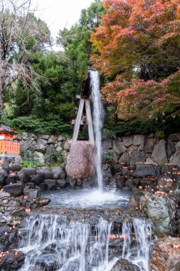 Bahçedeki kayaların üzerinde çağlayan sular, sonbahar renklerini gösteren ağaçlar. Küçük ışıklar suyun kenarına dizilir ve bu açık havada sıcak bir ortam yaratır..